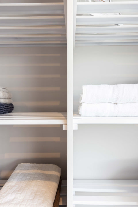 A set of white powder-coated aluminum linen shelves with multiple slats, mounted in an interior setting with towels and linen displayed.