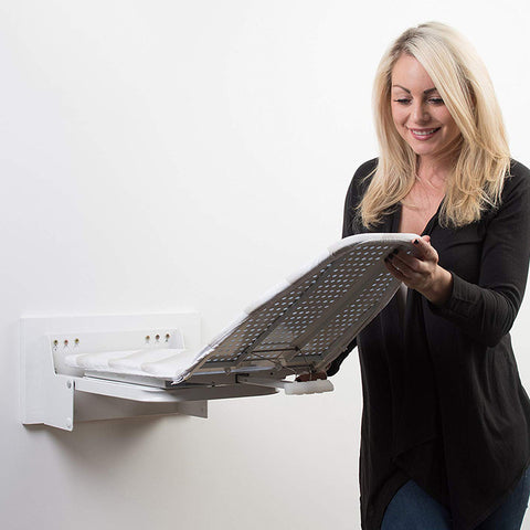 A person is smiling while using a wall-mounted swivel ironing board, which is white, in a room with a white wall in the background.